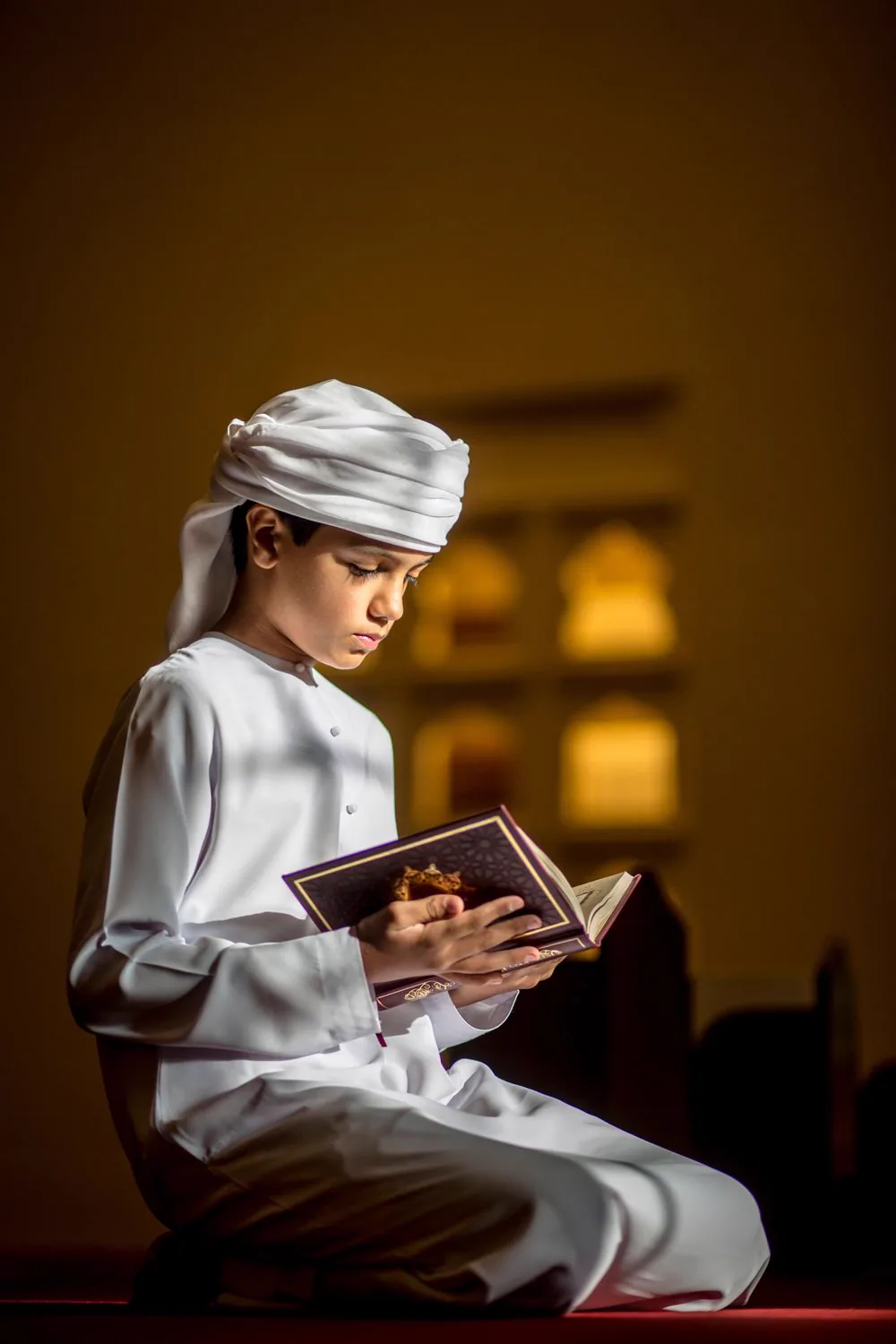 Boy in white traditional clothing reading a Quran